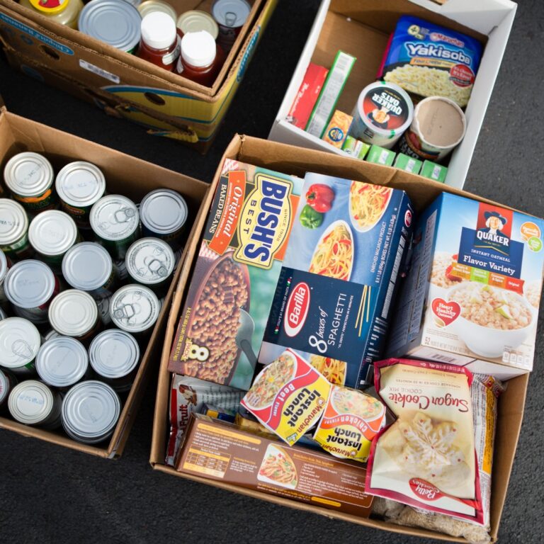 A bird's eye view shows open cardboard boxes filled with non-perishable food items, such as baked beans and oats.