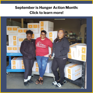 Three women smile in front of boxes of food donations.