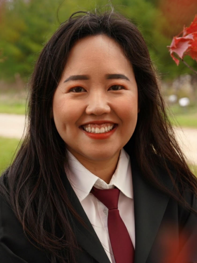 A smiling girl with long dark hair wearing a black blazer, white button-up shirt and a maroon tie.